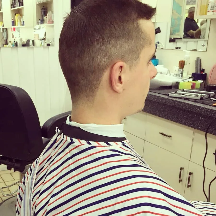 The barber reflected in the shop mirror — barber station, product shelves and the room behind him