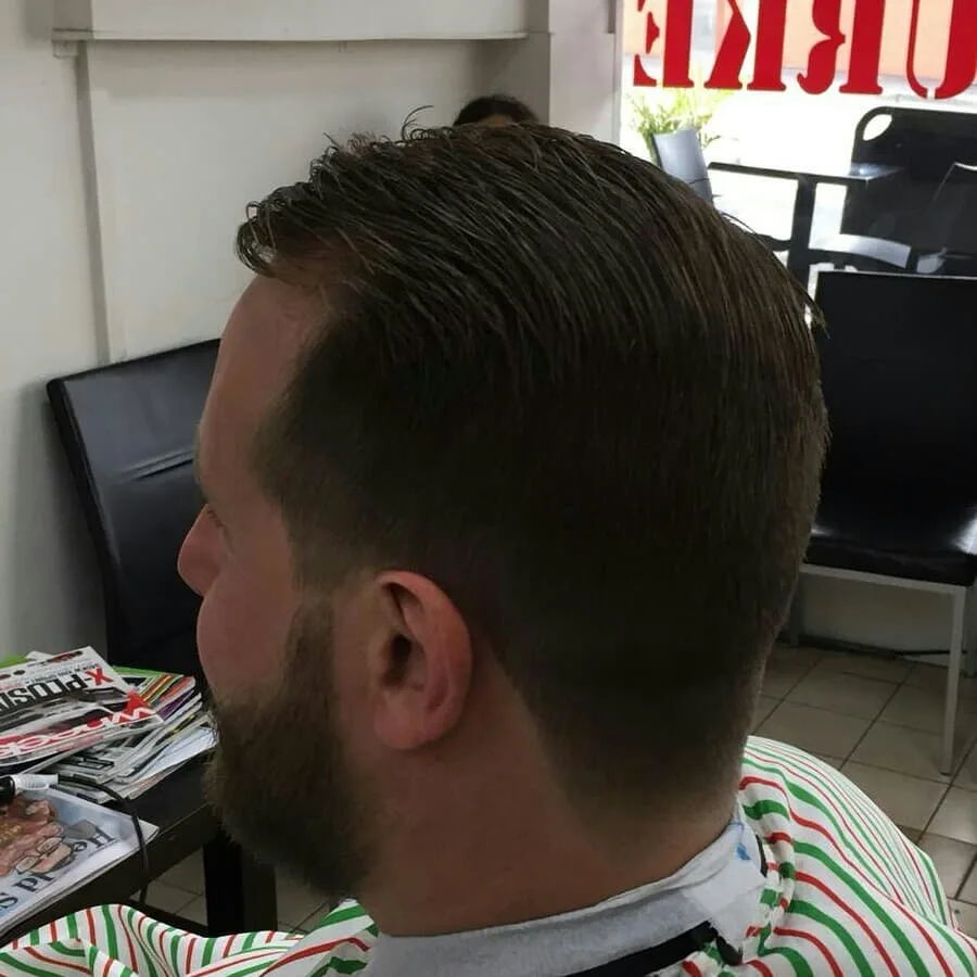 Back of head: slicked-back fade and beard; storefront window with Burke Road signage