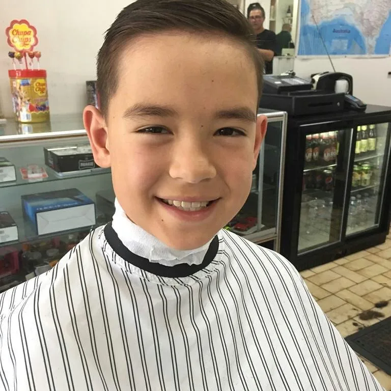 Young boy with fresh side-part cut, striped cape, in the barbershop