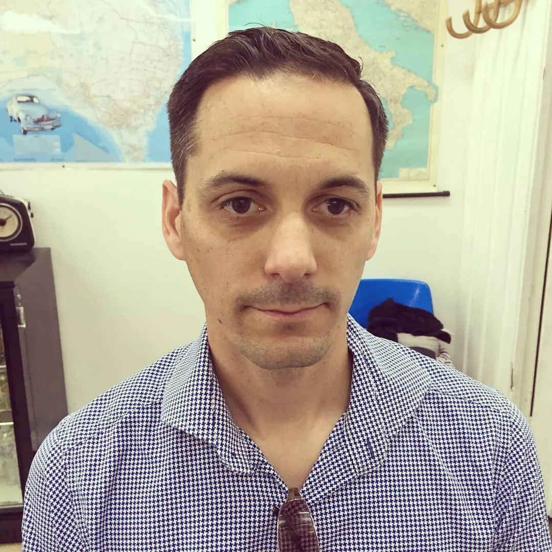 Man with neat short cut in blue houndstooth shirt, map of Italy behind